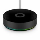 En svart, rund smart hub med blank ovansida och cirkul�r LED-ring som lyser i gr�nt och bl�tt, h�nger i kabel mot ljus bakgrund