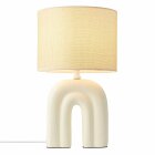 En bordslampa med beige tygsk�rm och en skulptural fot i b�gformad design st�r framst�lld och sprider ett mjukt ljus. Elbutik.se erbjuder denna stilfulla lampa som kombinerar modern form med varm belysning.