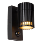 En svart v�gglampa med cylindrisk ribbad sk�rm �r monterad p� ett rektangul�rt v�ggf�ste med integrerad r�relsesensor. Elbutik.se erbjuder armaturen f�r automatisk och energieffektiv belysning vid entr�er, fasader och andra utomhusmilj�er.