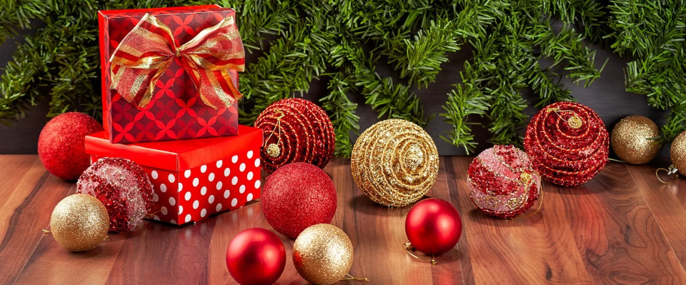 R&ouml;da julpaket med guldband och r&ouml;da och guldf&auml;rgade julgranskulor framf&ouml;r granris p&aring; en tr&auml;yta.